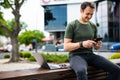 Attractive confident young man sitting on a bench outdoors at the city street, working on laptop computer, using mobile phone Royalty Free Stock Photo