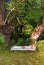 Attractive, content, young, sexy blonde woman lying in Bed in the under nature two old weeping willow trees