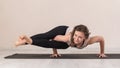 Attractive contented woman in sportswear practicing yoga performs Ashtavakrasana exercise, handstand against a wall background