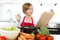 Attractive cook woman preparing vegetable stew soup reading recipe cookbook at domestic kitchen Royalty Free Stock Photo