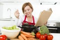 Attractive cook woman preparing vegetable stew soup reading recipe cookbook at domestic kitchen Royalty Free Stock Photo