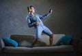 Attractive and cool happy man playing air guitar listening to music with yellow headphones holding mobile phone jumped on top of