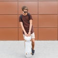 Attractive cool young hipster man in shorts in dark sunglasses in a fashionable t-shirt with a backpack is standing Royalty Free Stock Photo