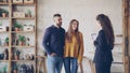 Attractive couple is discussing real estate deal with female realtor standing inside beautiful house, looking around and Royalty Free Stock Photo