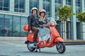 An attractive couple, a handsome man and female riding together on a red retro scooter in a city. Royalty Free Stock Photo