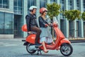 An attractive couple, a handsome man and female riding together on a red retro scooter in a city. Royalty Free Stock Photo