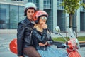 An attractive couple, a handsome man and female riding together on a red retro scooter in a city. Royalty Free Stock Photo