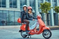 An attractive couple, a handsome man and female riding together on a red retro scooter in a city. Royalty Free Stock Photo