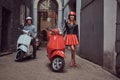 Attractive couple, a handsome man and female standing on an old street with two retro scooters. Royalty Free Stock Photo