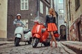 Attractive couple, a handsome man and female standing on an old street with two retro scooters. Royalty Free Stock Photo