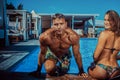 An attractive couple, handsome muscular male and woman sitting near the pool and enjoying a vacation. Royalty Free Stock Photo