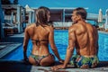 An attractive couple, handsome muscular male and woman sitting near the pool and enjoying a vacation. Royalty Free Stock Photo