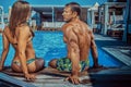 An attractive couple, handsome muscular male and woman sitting near the pool and enjoying a vacation. Royalty Free Stock Photo