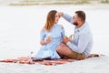 Attractive couple sitting together, looking each other, happy couple enjoying picnic on the white sand beach and drinking wine or Royalty Free Stock Photo