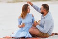 Attractive couple sitting together, looking each other, happy couple enjoying picnic on the white sand beach and drinking wine or Royalty Free Stock Photo