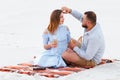 Attractive couple sitting together, looking each other, happy couple enjoying picnic on the white sand beach and drinking wine or Royalty Free Stock Photo