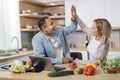 Attractive couple using laptop computer while preparing together healthy food giving high five