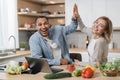 Attractive couple using laptop computer while preparing together healthy food giving high five