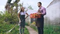 Attractive couple work near greenhouse. Man gardener in apron collect garbage in garden while his wife talking him Royalty Free Stock Photo