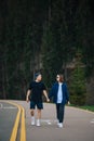 Attractive couple of young people walking on a mountain asphalt road in the woods holding hands. Romantic walk of man and woman on Royalty Free Stock Photo