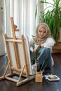 An attractive Asian-Muslim female artist sits on the floor in her art studio and paints on a canvas Royalty Free Stock Photo