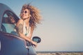 Attractive curly blonde young woman smile and enjoy the wind outside the car - concept of beauty and travel for happy and cheerful