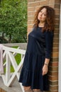 Attractive curly-haired red-haired woman for forty years standing on the porch of a country house in a blue dress with ruches. Royalty Free Stock Photo