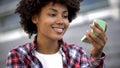 Attractive curly haired student looking in hand mirror, enjoying her appearance