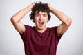 Attractive curly male scratches head and exclaims loudly, keeps mouth wide opened, wears casual t shirt, poses against white concr Royalty Free Stock Photo