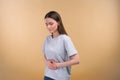 attractive dark haired woman keeps hands on stomach, suffers from discomfort, has spasm, dressed in shirt, over beige Royalty Free Stock Photo