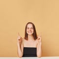 Attractive delighted brown haired woman wearing black top posing isolated over beige background pointing fingers upwards at copy Royalty Free Stock Photo