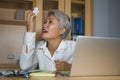 Attractive desperate and stressed middle aged Asian woman screaming gesturing overwhelmed and overwork working at office computer