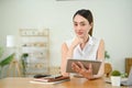 Determined Asian woman sits at the table with her digital tablet, hand on chin Royalty Free Stock Photo