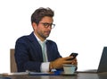 Attractive and efficient business man working at office laptop computer desk confident in smiling happy using mobile phone in succ Royalty Free Stock Photo