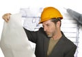 Attractive efficient and confident architect man in builder helmet checking building construction blueprints on design