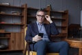 Attractive elderly grey haired man in glasses working on mobile phone, sitting on chair in office Royalty Free Stock Photo