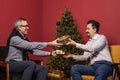 Attractive elderly man and his adult son exchanging Christmas presents gold boxes with ribbons