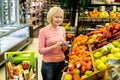 Attractive elderly woman choosing fruits at supermarket, holding notepad Royalty Free Stock Photo