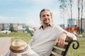 An attractive elderly 50-year-old man with long hair in the tail sits in a public garden on a bench. Warm summer day Royalty Free Stock Photo