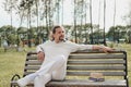 An attractive elderly 50-year-old man with long hair in the tail sits in a public garden on a bench. Warm summer day Royalty Free Stock Photo