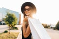 Attractive elegant girl, in a black dress and hat, wearing dark glasses, holding shopping bags and enjoying shopping, stands in Royalty Free Stock Photo