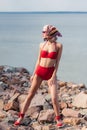 attractive elegant girl posing in red bikini and silk scarf on rocky beach