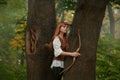 Attractive elven archer not ready to shoot a victim with a wooden bow arrow, a kind and sweet girl with long red hair in Royalty Free Stock Photo