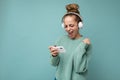 Attractive emotional positive young woman wearing blue sweater isolated over blue background wearing white bluetooth