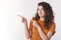 Attractive enthusiastic armenian young woman curly hair pointing looking intrigued left show index fingers awesome blank