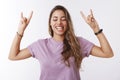 Attractive enthusiastic carefree european girl music festival fan raising hands showing rock-n-roll gesture tongue close