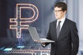 Attractive european businessman holding laptop with creative glowing Russian ruble hologram on blurry office interior background.