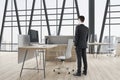 Attractive european businessman standing in modern concrete coworking office room interior with panoramic window and city view, Royalty Free Stock Photo