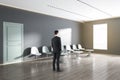 Attractive european businessman standing in modern waiting area interior with bright sunlight window, seats, door and wooden