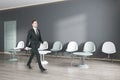 Attractive european businessman walking in modern waiting area interior with seats, door and wooden flooring. Policlinic and